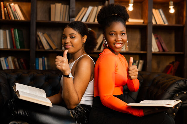 民族两个年轻的非洲女人在图书馆里用手势看书一起考试图书馆