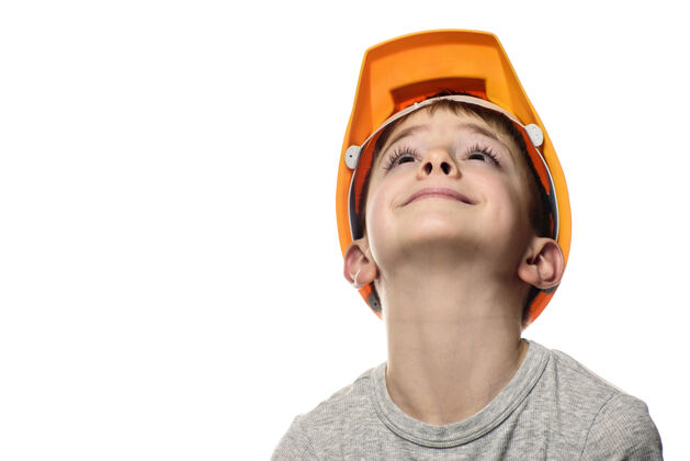 快乐戴橙色建筑头盔的男孩抬起头来向上纵向,面部隔离白色背景头盔教育橙色