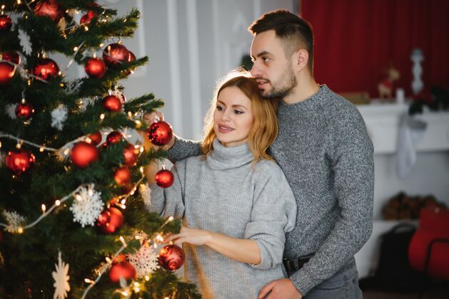 节日美丽的夫妇一起装饰圣诞树家庭年轻毛衣