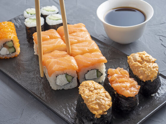 日本寿司各种各样的日本卷和寿司上有纹理的黑色侧板视图.竹子一卷筷子寿司卷鳄梨鱼子酱