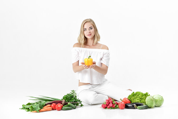 销售漂亮的金发女人 穿着白衣服 白色的桌子上放着很多新鲜蔬菜背景女孩拿着甜椒健康市场蔬菜
