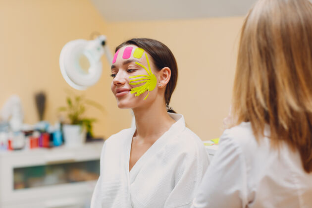 护理美丽的女人在脸上使用胶带提升治疗年轻化抗衰老美容