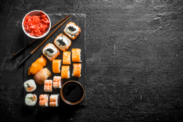 美味传统的日本寿司卷 在黑石头上放姜和酱油董事会黑色乡村餐桌美食鳄梨鲑鱼