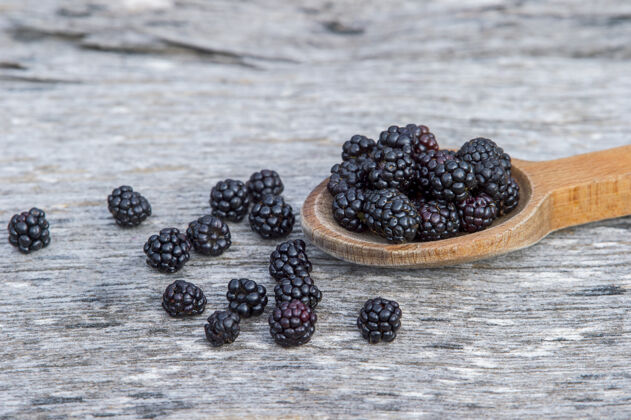 物体在古老的木制背景上 用木勺盛着成熟的黑莓多汁的大的成熟的黑莓