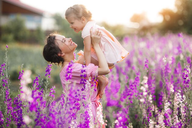 欢呼年轻漂亮的妈妈和她的小女儿一起在户外玩耍花紫罗兰色花坛女孩妈妈母性