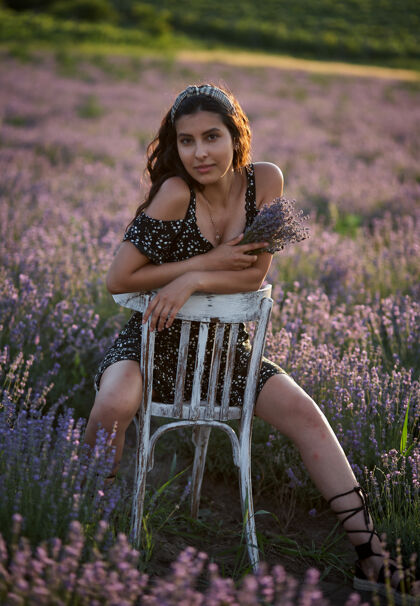 模特一位身穿黑色连衣裙的美女坐在一张木椅上 在一片薰衣草地的中央摆姿势美丽夏季魅力