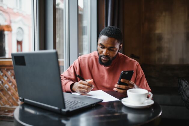 无线非洲年轻网店经理的个人资料照片 用手机与客户交谈工作工人咖啡
