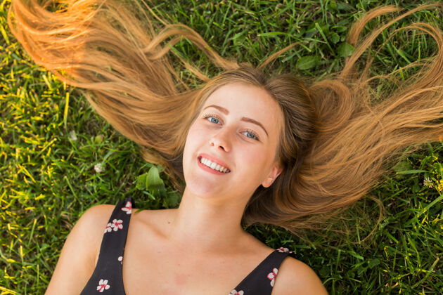 生活俯视图：一个快乐放松的女人躺在绿草上微笑着春天美丽假期