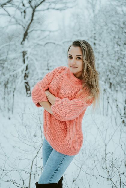 裤子一个穿着粉色宽松毛衣和牛仔裤的漂亮女孩在寒冷的雪域森林里公园雪花微笑
