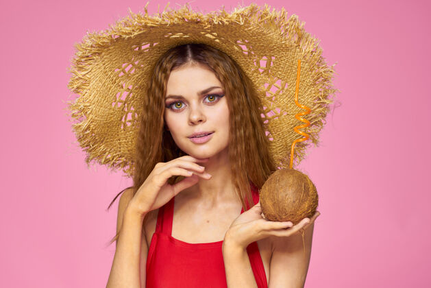 欢呼戴着草帽的椰子鸡尾酒的女人异国情调的度假夏日粉色的墙壁帽子成人姿势