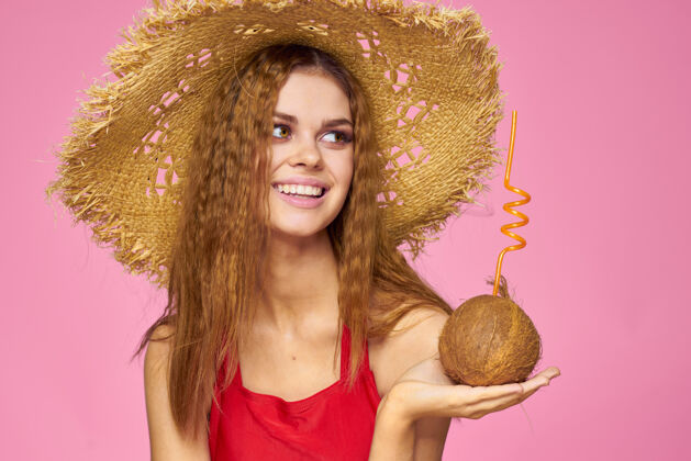 饮料戴着草帽的椰子鸡尾酒的女人异国情调的度假夏日粉色的墙壁时尚女人泳装