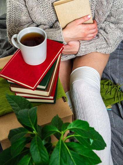 书房一个穿着毛衣的女孩一边喝茶一边看书很高兴见到你女孩用旧书分析家里的图书馆饮料假期智能