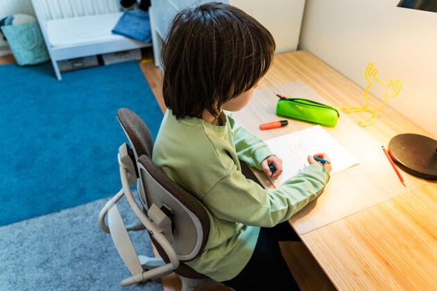 学校一个年轻的男生坐在手术台的矫形椅上做作业家集中儿童写作家庭教育概念桌子专注钢笔
