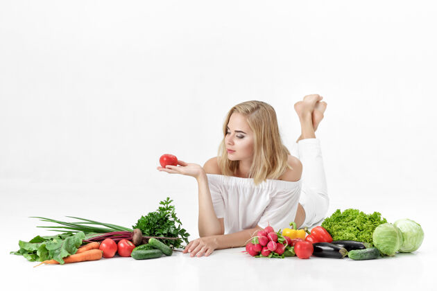 市场漂亮的金发女人 穿着白衣服 白色的桌子上放着很多新鲜蔬菜背景女孩拿着西红柿女人绿色饮食