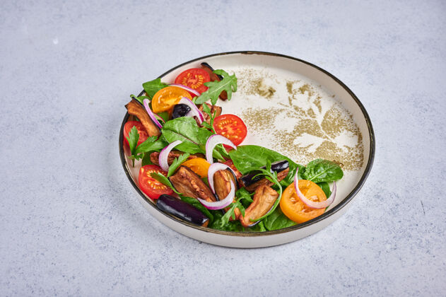 叶子自制风格沙拉与炒茄子 西红柿 芝麻菜 菠菜 生菜和酱汁在一个陶瓷盘子生的美味生菜