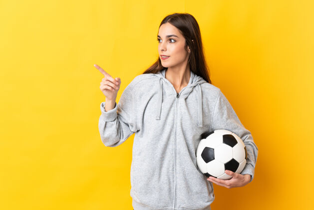 年轻一个年轻的足球运动员女人被隔离在黄色的背景下 一边想一边举手一边实现解决方案快乐表达足球