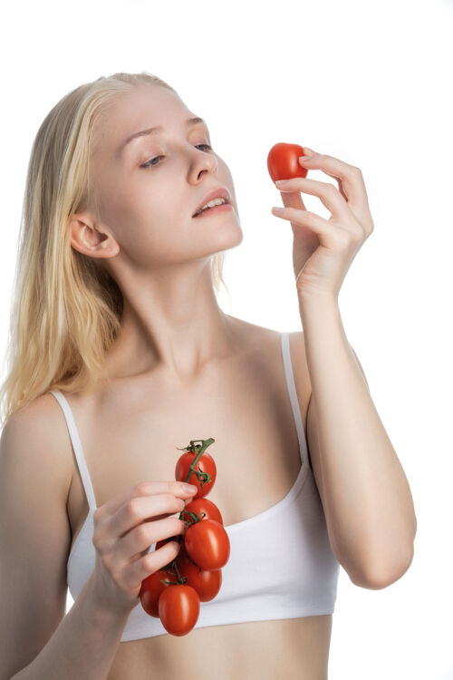 饮食一个金发碧眼的白衣女人胸罩她的左手拿着一个西红柿 把她的手举到脸的高度身材内衣锻炼