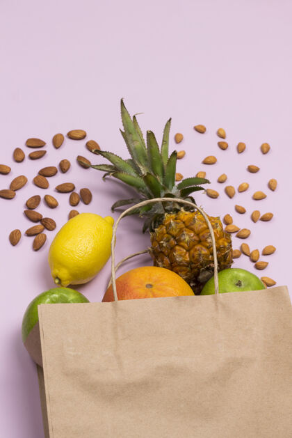 杏仁粉红色背景上有水果 苹果 柠檬 葡萄柚 菠萝和坚果的纸袋多汁的维生素花生