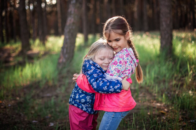 友谊可爱的女孩在秋天的森林里散步 用爱和温柔拥抱着她的小妹妹 全国拥抱和友谊日 休闲的生活方式 户外两姐妹女孩支持