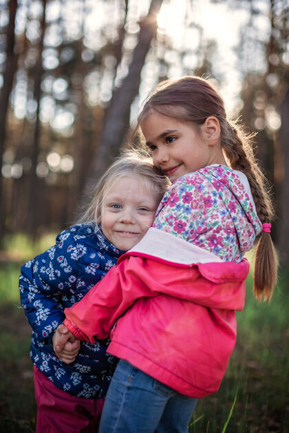 在一起可爱的女孩在秋天的森林里散步 用爱和温柔拥抱着她的小妹妹 全国拥抱和友谊日 休闲的生活方式 户外善良纽带积极