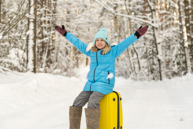 行李冬天 一个穿着毡靴的女孩在一个寒冷的雪天坐在手提箱上包坐着手提箱