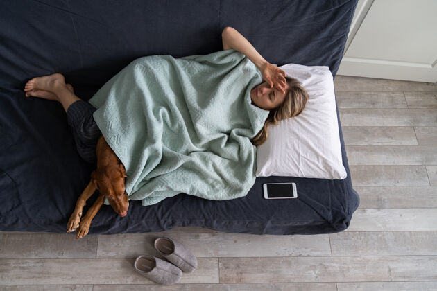 枕头疲惫不堪的女人躺在床上 家里养着狗 患有剧烈的紧张性头痛 偏头痛 流感疼痛里面疲惫