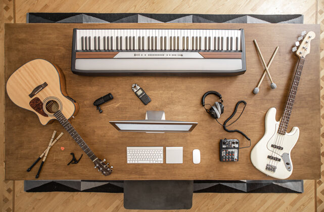 乐器一张大木桌上放着一把原声吉他 低音吉他 音乐键 棍子 带音乐混音器的耳机 卡帕达斯特和电脑吉他唱片创作