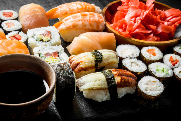 Maki各种各样的面包卷 寿司和maki放在一块石板上 上面放着酱油和生姜生的食品虾