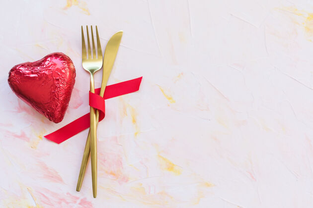 食谱红色丝带上的金色餐具和粉红色的红色箔上的巧克力心餐具庆祝箔材