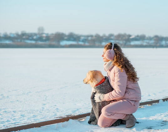 季节冬日冰河上的年轻女子和她的金毛狗坐在一起猎犬女人在户外和狗玩年轻金毛猎犬天气