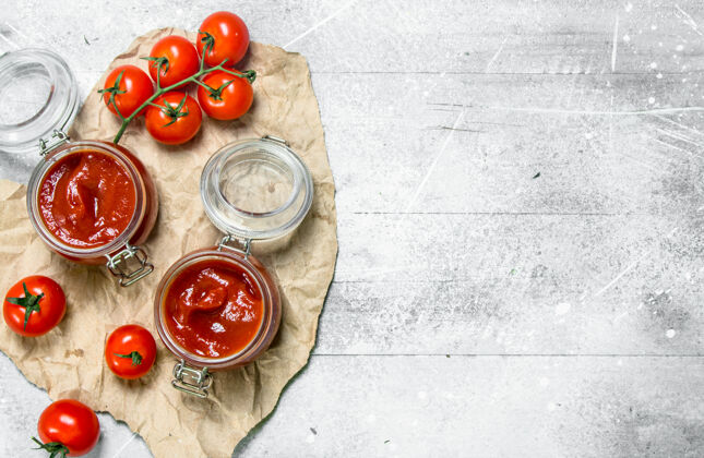 菜肴番茄酱放在一个玻璃罐里 放在纸上和樱桃上食物礼服自然