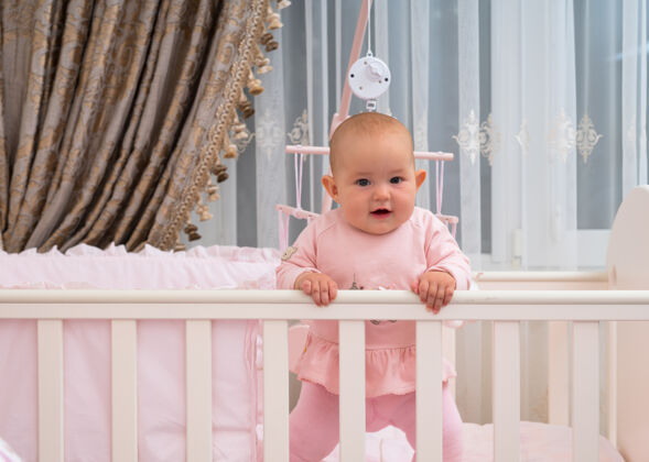智力一个快乐 欢笑的女婴站在婴儿床上的粉色卧室场景关注肖像可爱