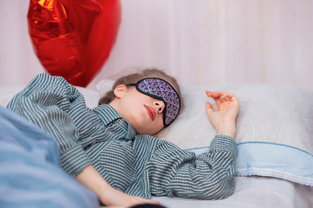 长发一个年轻健康的女人睡在床上 戴着睡眠面罩和睡衣梦人房间