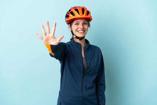 计数一个骑自行车的年轻女子被隔离在蓝色背景下 用手指数着五个年轻年轻骑