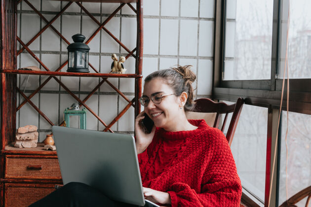 购物一个年轻的女人微笑着 一边在他的笔记本电脑上工作 一边在一个独立的现代住宅上打电话教师个人大流行