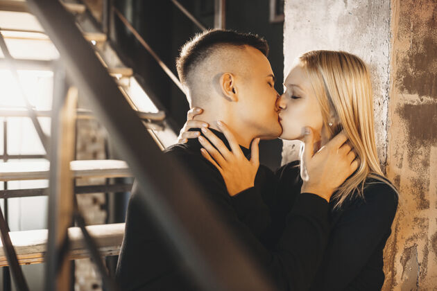 情人节一对可爱的年轻夫妇坐在家里的楼梯上 在温暖的灯光下亲吻的画像舒适人女人