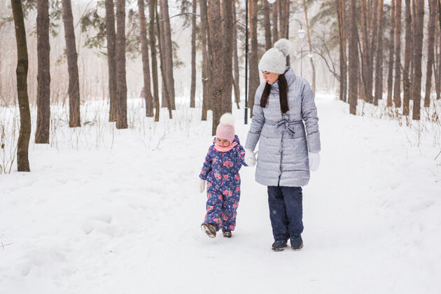 孩子家庭 冬天和自然的概念-年轻开朗的母亲带着可爱的小女儿走在街上户外妈妈家庭
