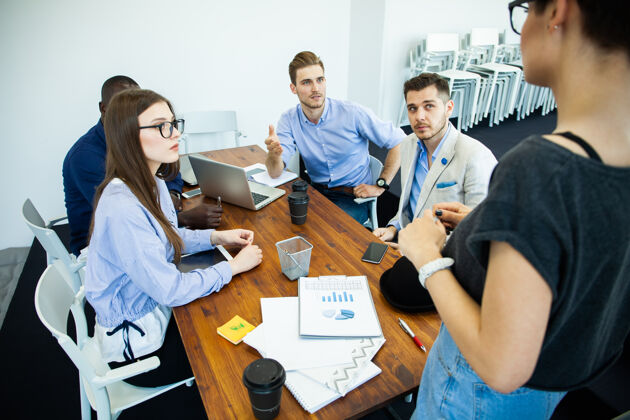团体讨论成功项目组年轻开朗的商务人士坐在办公桌前与坐在后台的同事一起工作和交流团队年轻自信