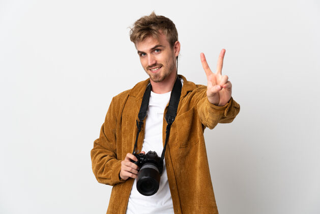 人年轻的摄影师金发男子孤立在白色微笑和显示胜利的迹象青年摄影师设备