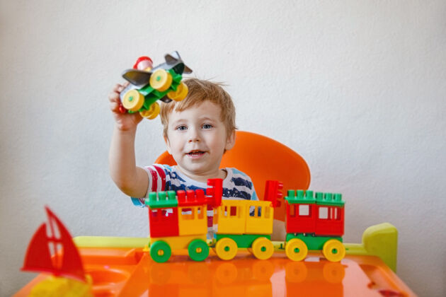 小一个金发小男孩坐在家里的书桌旁 手里拿着亮晶晶的塑料玩具 玩着拿着玩具的飞机向上向上高质量的照片技能教育交通