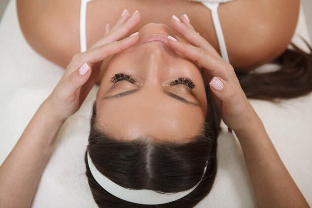 沙龙俯视图：一位女士在水疗中心放松 接受面部按摩护理专业治疗
