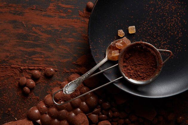 喜悦用勺子把糖果和可可粉放在一个黑盘子上的筛子里 黑面上放着巧克力零食诱惑配料