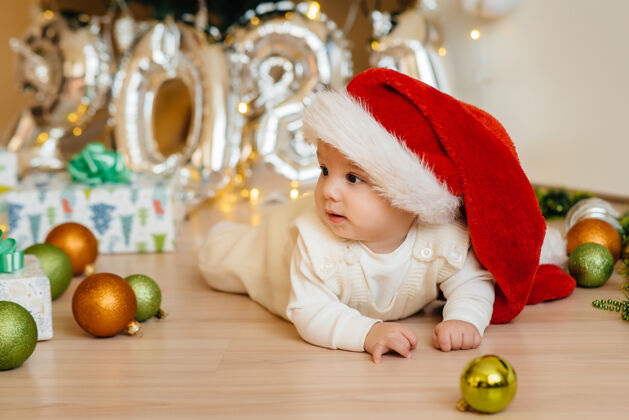 帽子可爱的微笑着的婴儿躺在圣诞树下和孩子们玩耍礼物.圣诞节还有新年庆祝活动礼物圣诞宝宝脸