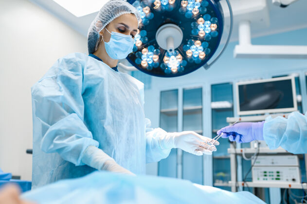 治疗手术室里穿着长袍戴着口罩的女外科医生 背景灯亮着手术医疗面部面罩