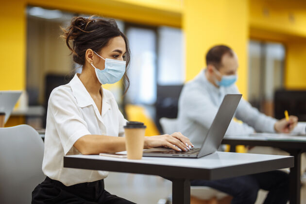 防护一位妇女在办公桌上用笔记本电脑工作 戴着医用口罩 在covid-19大流行期间保持安全医疗工人办公室