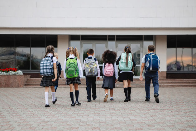 制服一群穿着制服 背着五颜六色背包的小学生排成一行站在教室前面学校回来查看高尔夫裙子操场