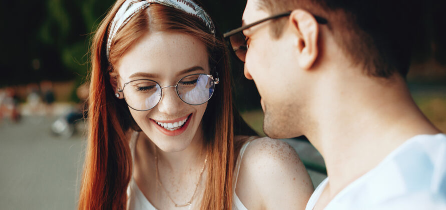 女性红发白种女人 满脸雀斑 戴着眼镜 在公园的长凳上和爱人欢笑微笑爱休闲