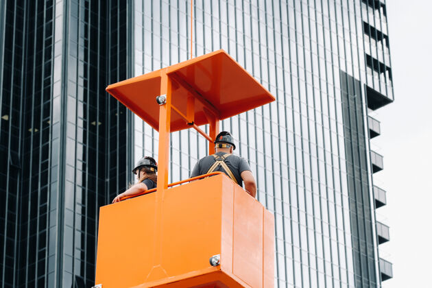 头盔工人们在一个建筑摇篮爬上起重机到一个大玻璃建筑牛仔裤团队起重机