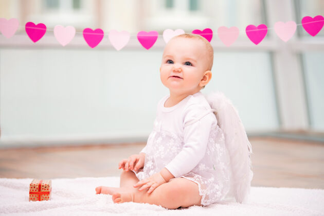 微笑一个快乐淘气的婴儿的肖像 长着白色天使的翅膀心天天使