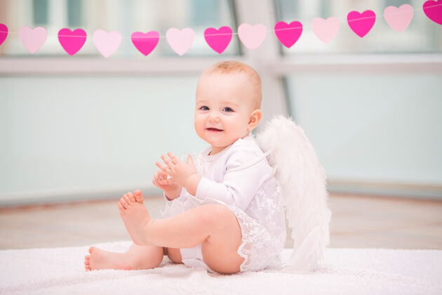 新生儿一个快乐淘气的婴儿的肖像 长着白色天使的翅膀花环小肖像
